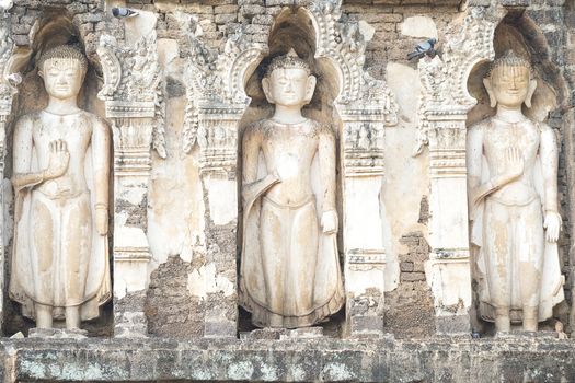 Three standing buddha statues on an ancient limestone pagoda at Wat Jammathevi, Meung, Lamphun, Thailand.