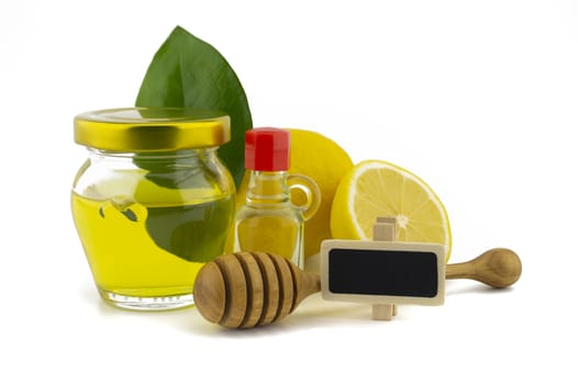 Honey and lemon still life for healthy diet concept with a wooden wand leaning on a glass jar of honey against green leaves and fresh halved juicy lemon over a white background