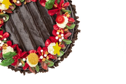 A chocolate cake decorated with red, white and green flowers and leaves, appropriate for Christmas and New Year celebration. Top view, closed up, isolated on white background with copy space.