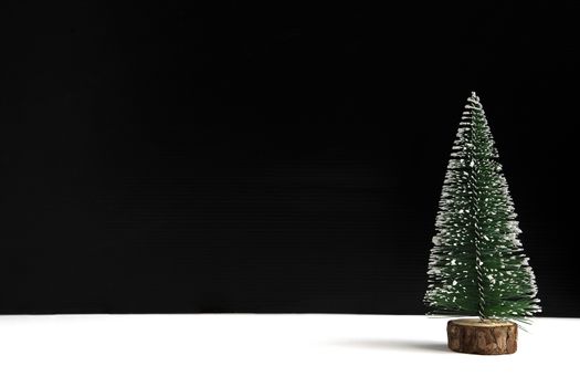 A miniature Christmas tree with faked snow on black and white background with copy space.