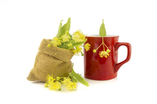 Red cup and small hessian bag of freshly picked yellow linden flowers and leaves, also called tilia and lime, for making a healing tisane or tea over a white background