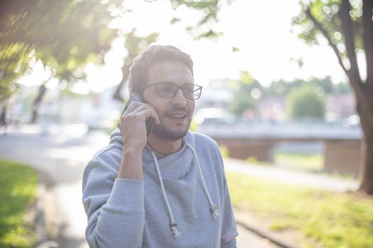 Good news and happy face - Man talking on smartphone in park, outdoor shoot, back light