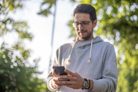 Smart looking man texting message on smartphone, outdoor park shoot, back light