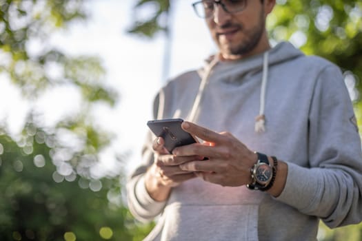 Smart looking man texting message on smartphone, outdoor park shoot, back light