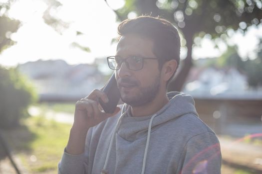 Man talking on smartphone in park, outdoor shoot, lens flare back light