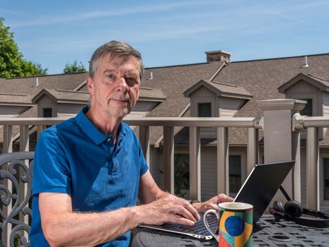 Senior caucasian man working from home during coronavirus epidemic using laptop and smiling at the camera