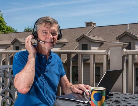 Senior caucasian man working from home during coronavirus epidemic using headset and laptop to communicate