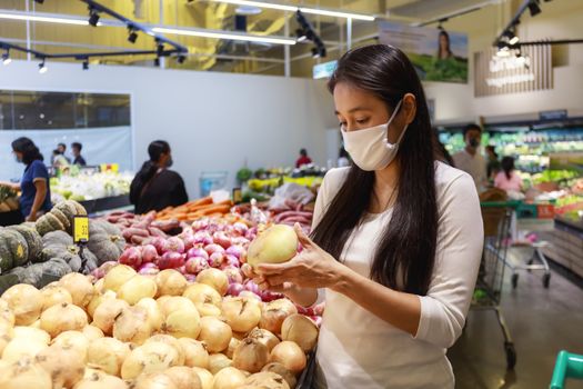 Asian woman wearing protective face mask push and hold shopping cart in supermarket department store. Girl, looking grocery to buy  some food. New normal after covid-19. Family concept.