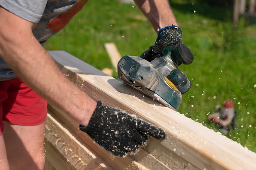 carpenter hands use an electric tool to process raw lumber