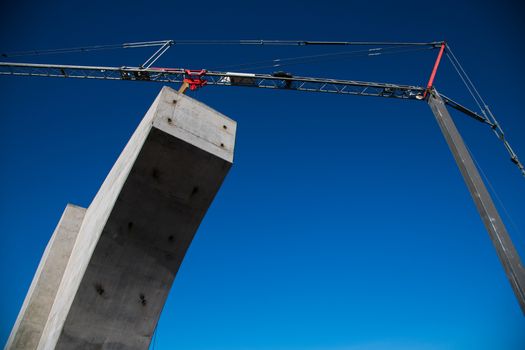 Construction of the interchange of a road bridge across the river. Builders and construction equipment on the construction site. The support of the bridge against the blue sky.