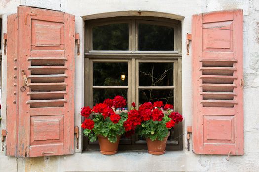 Old window with open shutters and geranium flower decoration