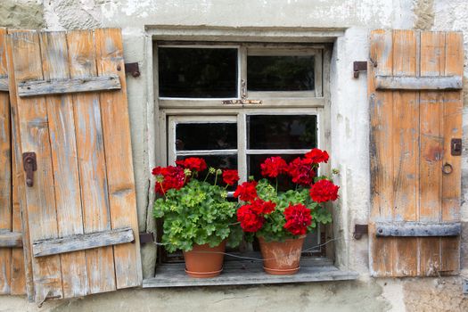 Old window with open shutters and geranium flower decoration