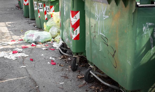 Trash cans standing in a row ready to be collected on a residential street. On the ground, garbage bags that create pollution and dirt.