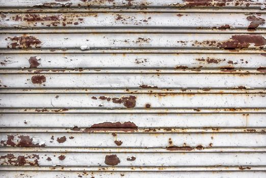 Old damaged white rolling steel door. A shutter totally rusted, closed by years.