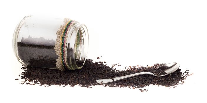 Isolated glass jar with fermented big leaves of ceylon tea on white background. On the side there is also a teaspoon