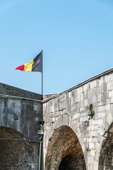 Dinant, Belgium - June 26, 2019:Dinant, Belgium - June 26, 2019: Seen insde Citadelle.  Closeup of Belgian flag on corner of gray stone ramparts against blue sky.