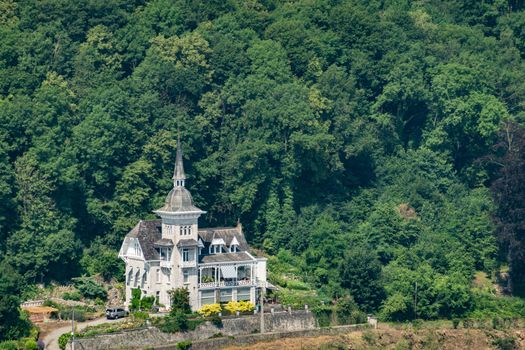 Dinant, Belgium - June 26, 2019: Seen from Citadelle. Focus on white gray historic mansion and villa set against green foliage of forest. Yellow flowers.