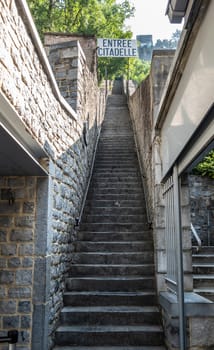 Dinant, Belgium - June 26, 2019: Entrance to the long naroow brown stone stairway up to the citadel, captured in green foliage. Closeup.