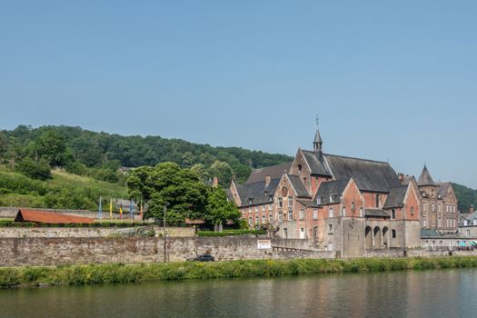 Dinant, Belgium - June 26, 2019: Part of Red stone ancient convent of the Capuchins is now the seat of CPAS, the social services of the city. Meuse River in front, blue sky.