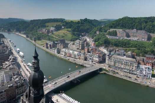 Dinant, Belgium - June 26, 2019: Seen from Citadelle. Charles de Gaulle bridge with focus on south flow of River Meuse. Green landscape, blue sky and plenty of buildings, Church spire.