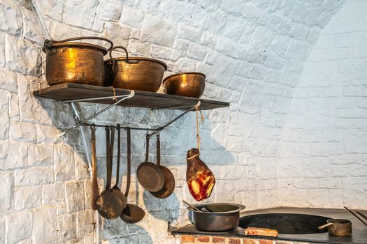 Dinant, Belgium - June 26, 2019: Inside Citadelle. Part of historic army kitchen with copper pots, ham and stove against white painted wall.