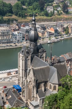 Dinant, Belgium - June 26, 2019: Seen from Citadelle. Bird eye view on Notre Dame church on River Meuse bank with cityscape and green foliage.