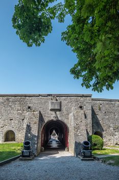 Dinant, Belgium - June 26, 2019: Inside Citadelle. Gray stoen Ramparts and gate to inner courtyard with rooms against blue sky, Green foliage.