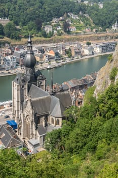 Dinant, Belgium - June 26, 2019: Seen from Citadelle. Bird eye view on Notre Dame church and cliff on River Meuse bank with cityscape and green foliage.