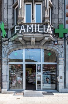 Dinant, Belgium - June 26, 2019: Facaden wity display windows of familia pharmacy on Place Reine Astrid shows Green crosses and drug advertisements in window.
