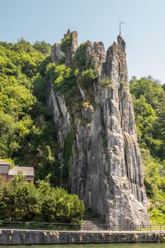 Dinant, Belgium - June 26, 2019: Le rocher Bayard along La Meuse River surrounded by green foliage under blue sky.