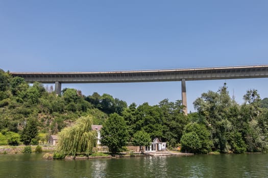 Dinant, Belgium - June 26, 2019: Very high Route Charlemagne, N97, concrete bridge over Meuse River under blue sky with green Ile d’ Amour and its lone building in center of river.