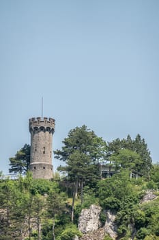 Dinant, Belgium - June 26, 2019: Brown stone watch tower of Citadelle fortification under blue sky on top of rocks and surrounded by green foliage.