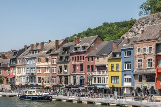 Dinant, Belgium - June 26, 2019: Part of Row of colorful business facades just past Charles de Gaulle bridge on norht right bank of Meuse River under blue sky.