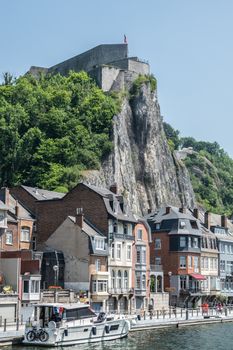 Dinant, Belgium - June 26, 2019:Seen from north right bank with businesses and houses, Citadelle front top with Belgian flag and people.