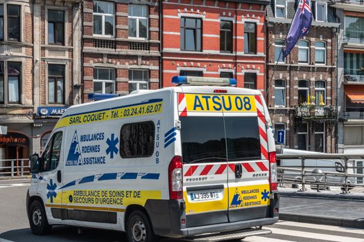 Dinant, Belgium - June 26, 2019: White and yellow ambulance van on Charles de Gaulle Bridge. Pubs and restaurants in back.