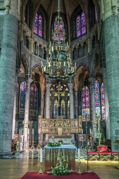 Dinant, Belgium - June 26, 2019: Inside Collégiale Notre Dame de Dinant Church. Main altar with giant chandelier and stained glass windows. Reredos of paintings.