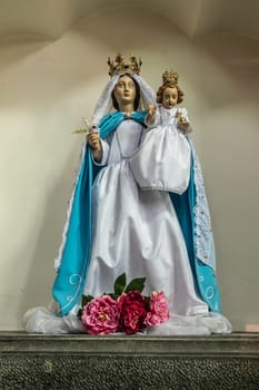 Dinant, Belgium - June 26, 2019: Inside Collégiale Notre Dame de Dinant Church. Closeup of Painted statue of Notre Dame, Our Lady as madonna, mother and child. Red flowers on feet.