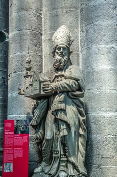 Dinant, Belgium - June 26, 2019: Inside Collégiale Notre Dame de Dinant Church. Gray stone statue of Belgian medieval Saint Materne against pillar. Red sign with history.