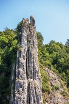 Dinant, Belgium - June 26, 2019: Frontal view. Le rocher Bayard along La Meuse River surrounded by green foliage under blue sky.