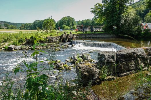 Han-sur-Lesse, Belgium - June 25, 2019: Green landscape with rapid on Lesse River when it leaves the Grottes-de-Han cave system.  Forested hills and people.