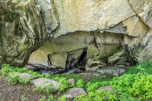 Han-sur-Lesse, Belgium - June 25, 2019: Grottes de Han. Spot where Lesse River enters the cave system. Light colored rocks and some green vegetation.
