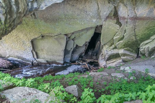 Han-sur-Lesse, Belgium - June 25, 2019: Grottes de Han. Spot where Lesse River enters the cave system. Light colored rocks and some green vegetation.