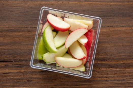 green and red apples are cut into pieces and placed in a clear box ready to be eaten , food delivery concept