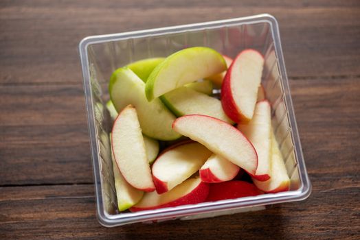 green and red apples are cut into pieces and placed in a clear box ready to be eaten , food delivery concept
