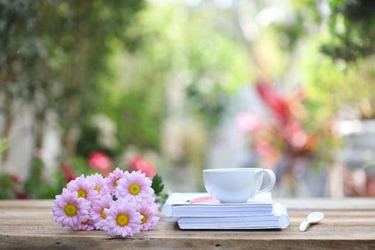 White coffee cup with white notebook and pink pencil with pink Chrysanthemum flower on wooden table at outdoor