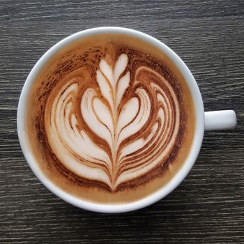 Top view of a mug of latte art coffee on timber background.