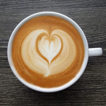 Top view of a mug of latte art coffee on black background.