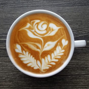 Top view of a mug of latte art coffee on black background.