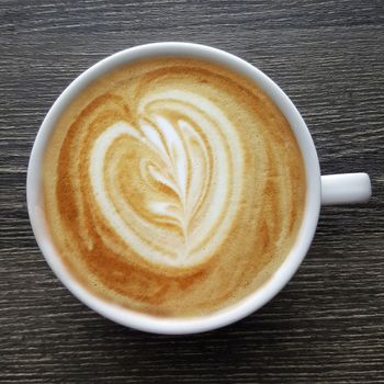 Top view of a mug of latte art coffee on black background.