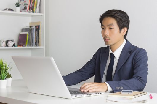 Portrait Asian Businessman in Formal Navy Blue Suit Using Laptop and Working in Office. Asian businessman with laptop and smartphone